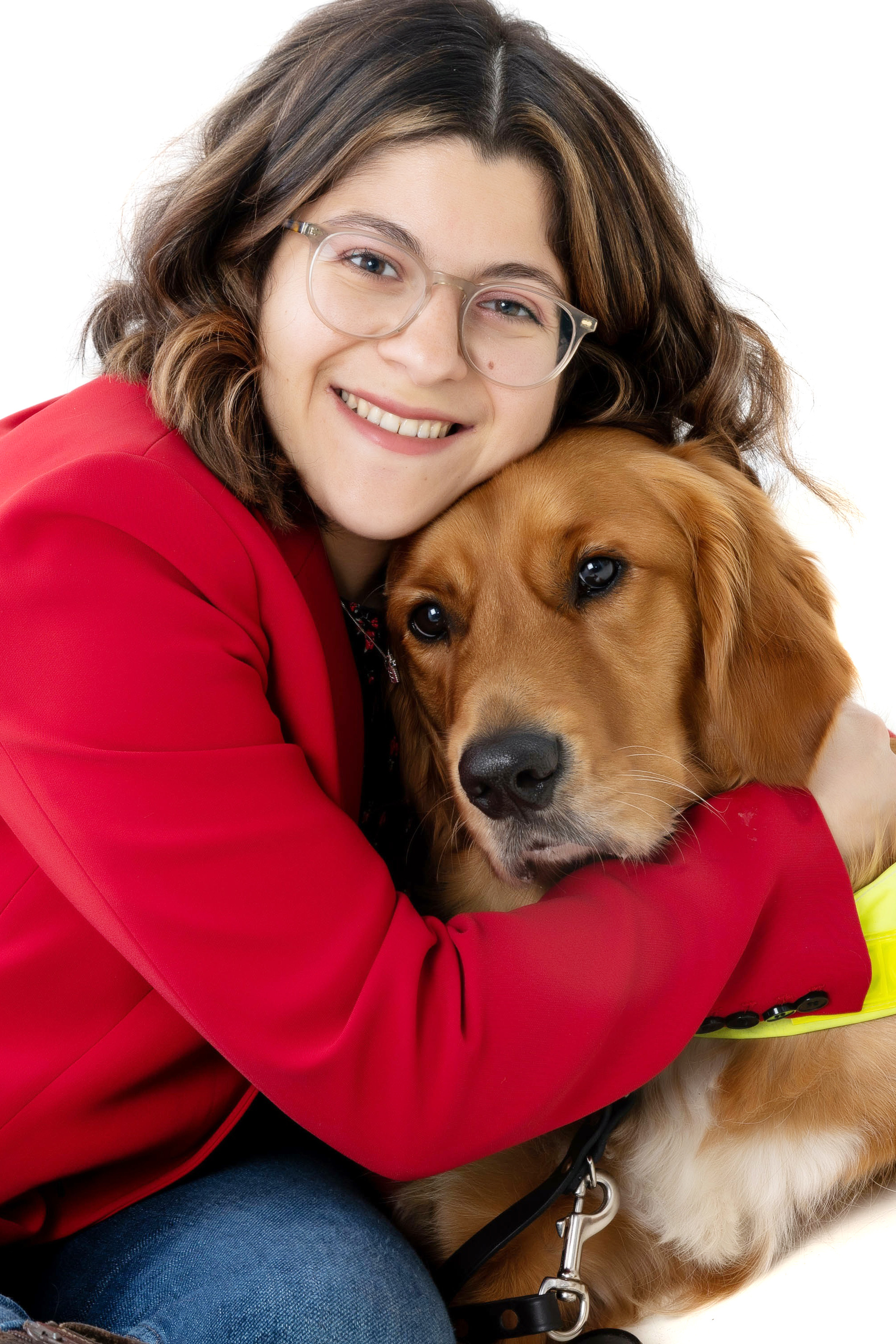 Zein is wearing a red suite jacket and she is hugging her guide dog Mitch who is a fox colored Golden Retriever/