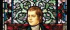 Stained glass window with a portrait of Robert Burns on a floral background and the name 'Burns' in the window above his head. Source: University of Glasgow https://www.gla.ac.uk/events/globalburns/