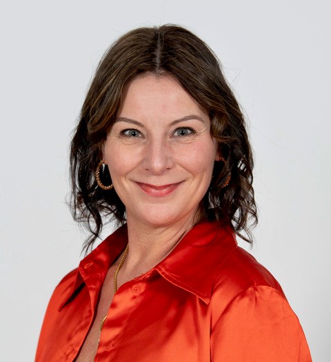 A head and shoulders shot of Lynn Stewart smiling in a bright top set against a plain grey background