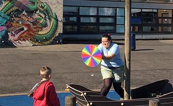 Photograph showing a member of the Shedload team spinning a colourful wheel in front of a school pupil. 
