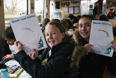 Photograph of two girls holding up their worksheets to show off the drawings they have done. 