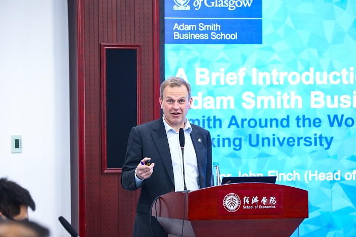 A man speaking at a podium with a banner behind him which says 'Adam Smith Business School. Smith Around the world. Peking University '.Source: Peking University