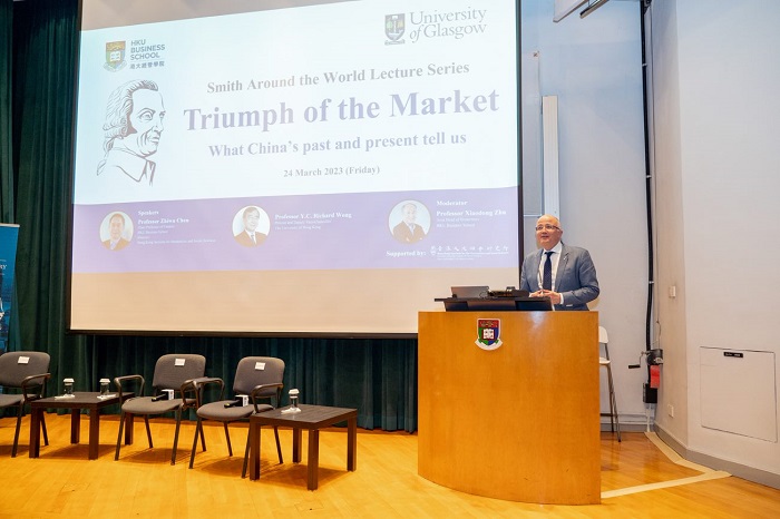 A man at a podium with a screen showing a slide with text 'Triumph of the Market: What China’s past and present tell us'. Source: Hong Kong University