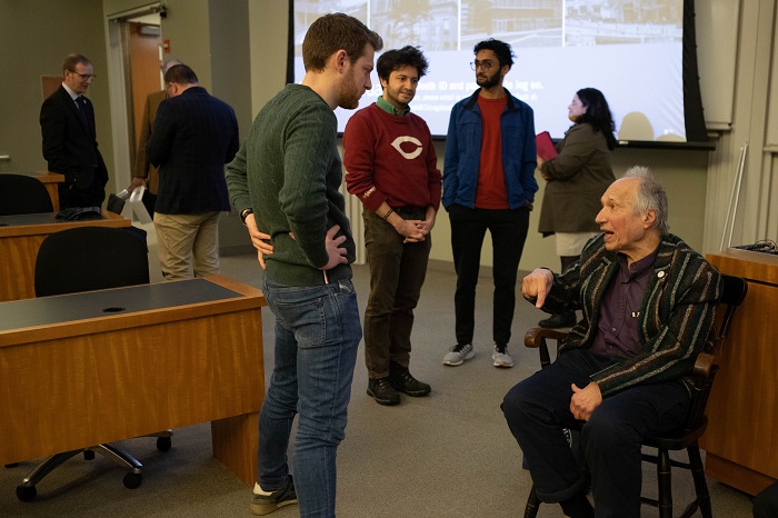 Sam Feltman speaking to a student in front of him with a few in the background also listening in to the discussion Close-up on Sam Peltzman's animated face and raised hands while he is speaking to a person whose face can't be seen. Source: Chicago Booth University