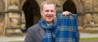 Professor John Finch smiling and holding up an Adam Smith tartan lambs wool scarf