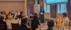 An event with groups of people at round dinner tables with white tablecloths and candles listening to a woman giving a talk. Source: University of Glasgow