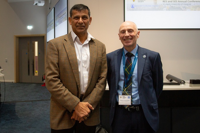 Two people standing together in a lecture theatre where behind them are the presentation slides on white board. Source: University of Glasgow