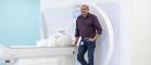 Dr Shajan Gunamony holds the 7T Head Coil beside the 7T MRI scanner