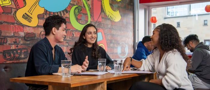 QMU students sitting at table in front of graffiti wall backdrop 