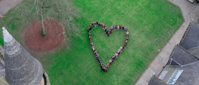 Aerial view of people collected in the outline of a heart shape on the grass in the quadrangle of gilbert scott building