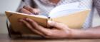 Close up partial portrait of black female author at home writing in journal. 