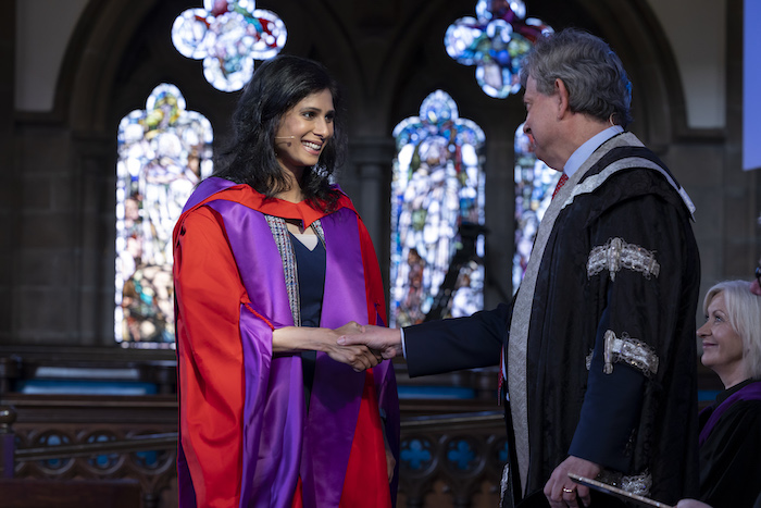 Gita Gopinath, dressed in purple and red academic robes, smiles as she shakes hands with Glasgow University principal Anton Muscatelli 