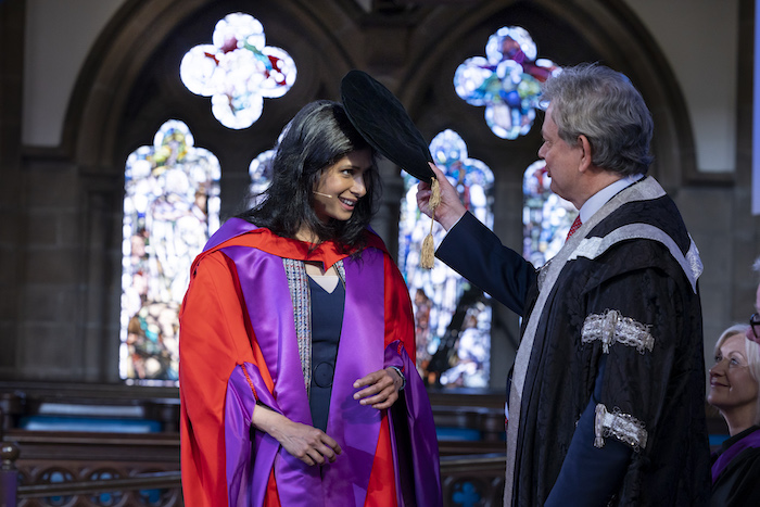 Glasgow University principal Anton Muscatelli taps Gota Gopinath on the top of the head with an academic cap to award the honorary degree. The are both wearing academic robes: Gita Gopinath's are red and purple and Anton Muscatelli's are black and silver
