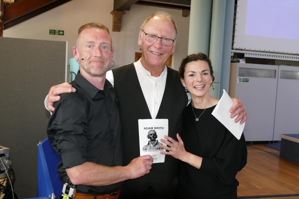 Image of the three people from the In company theatre productions from their performance the life and times of Adam Smith. All holding the script in between the with Adam Smith's face. Source: ASBS