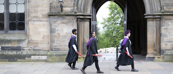 Students in gowns with scrolls walk in the quadrangle during graduation