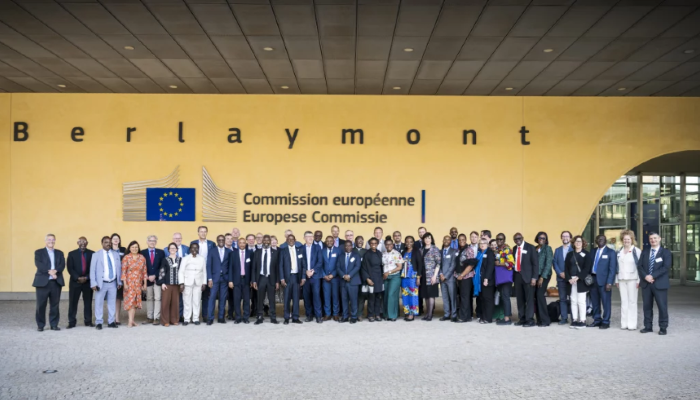 A group of dignitaries stood in front of a yellow wall and an EU Commission logo