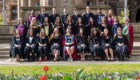 A mix of students and academics sat and stood in three rows outside in graduation attire outside the UofG main building