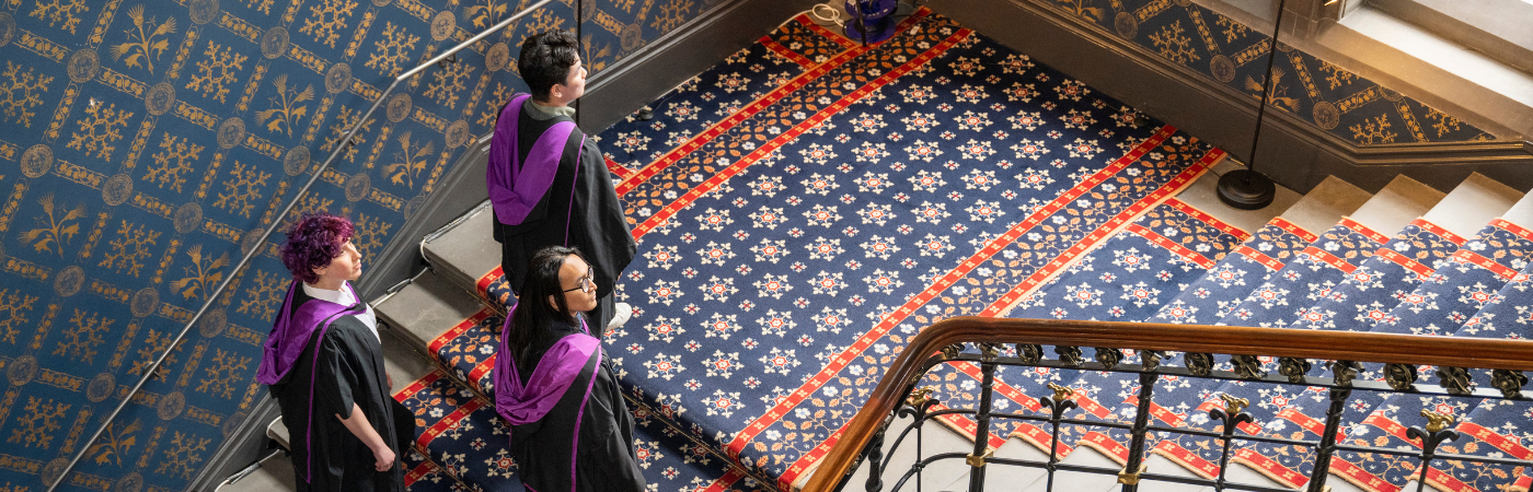 A group of three graduating students in gowns, ascending stairs to Bute hall