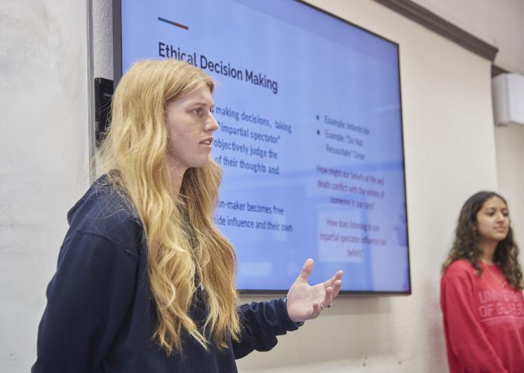 Student standing giving a presentation with powerpoint slide with the title Ethical Decision Making. With another presenter at the other side. Source: Charlotte Morris External Relations 