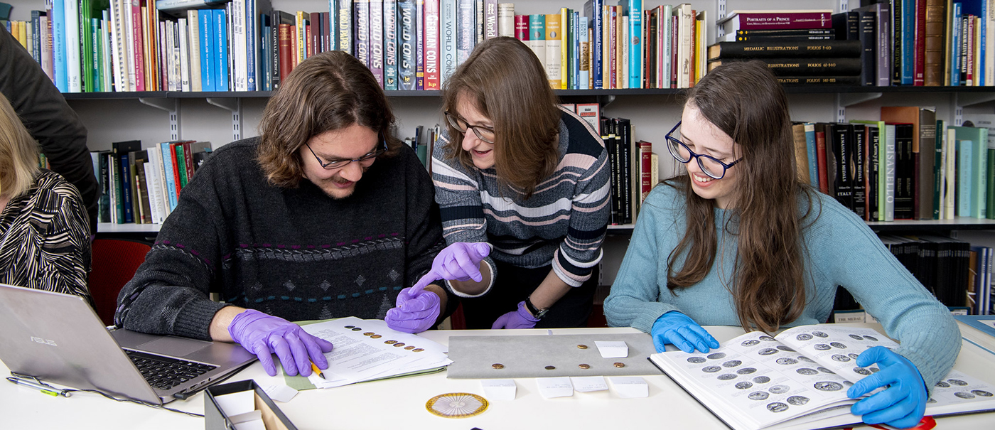 Students examining ancient coins with the help of a tutor
