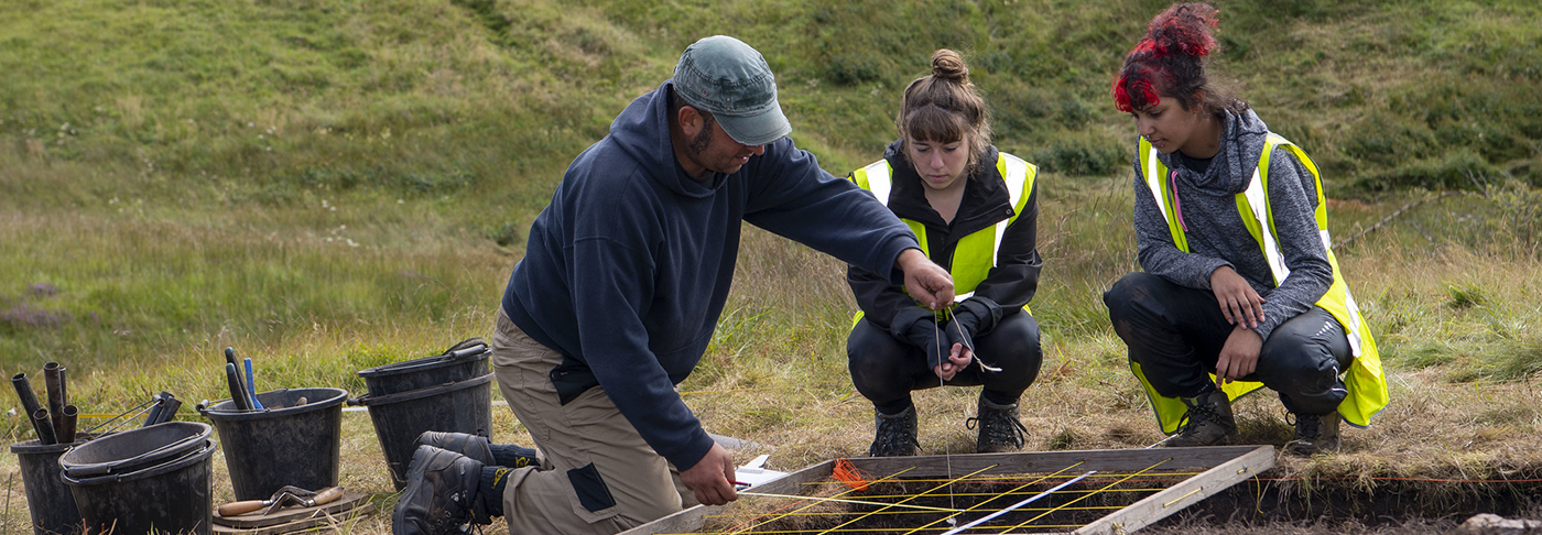 A tutor showing students on archaeological fieldwork how to use a planning frame. 
