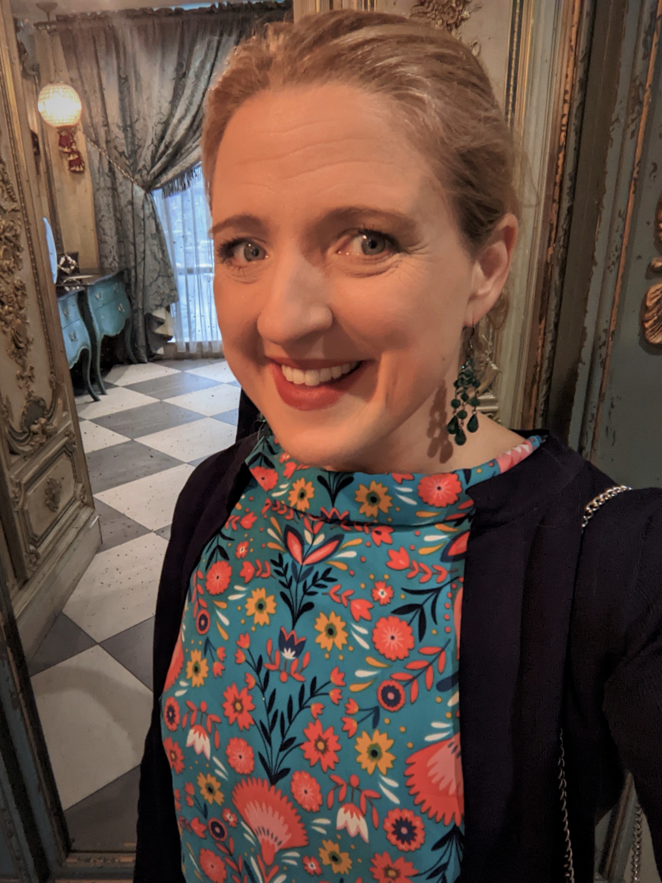 Headshot of a woman in a floral jumpsuit standing in an elaborate doorway