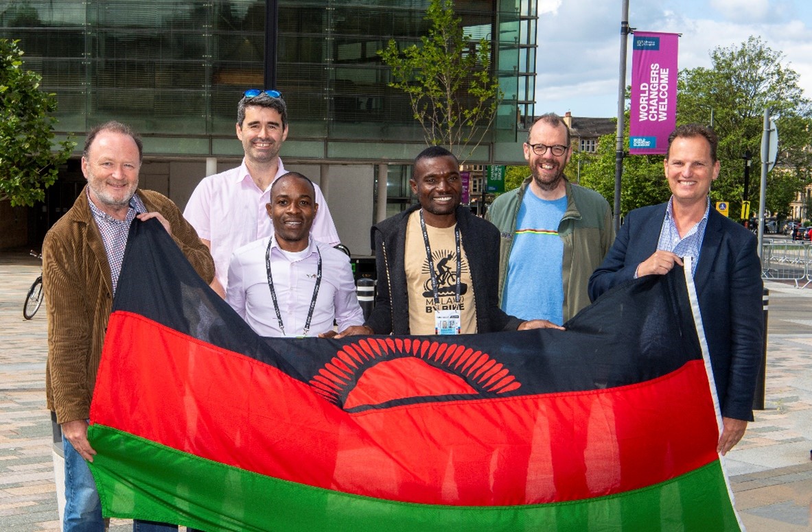 Prof Mike Barrett, Prof Stuart Gray, Malombo Kayira, MacPherson Mbeya stood together on campus holding a Malawi flag in front of them