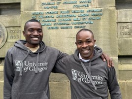Macpherson Mbeya and Malombo Kayira standing with arms around each other in front of the UofG main building