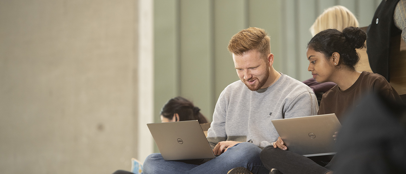 Two students with laptops having a conversation