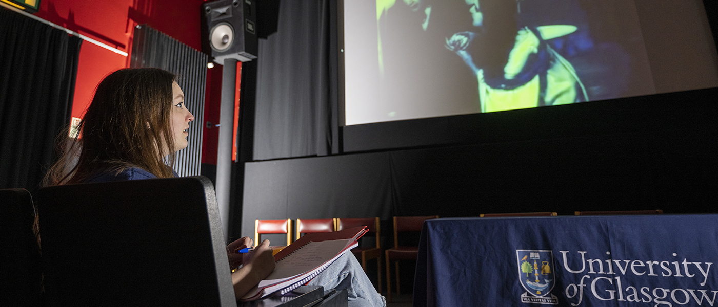 A student takes notes while watching a film on a cinema screen