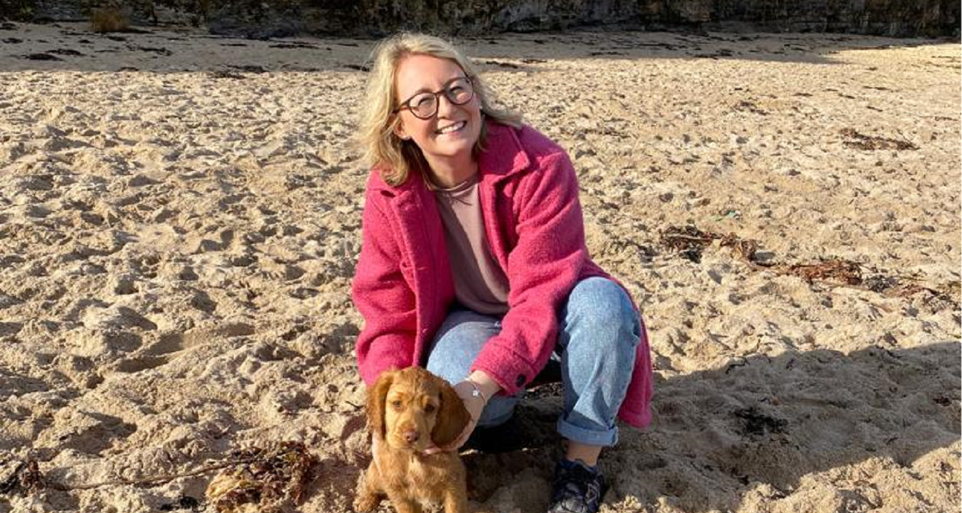 Photo of UofG staff member Margaret Thomson standing on a beach with a tiny puppy