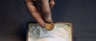 a close up photo of a hand holding a small gold coin above a trinket box full of white salt