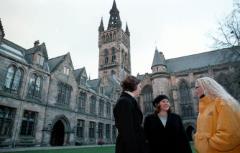 outside scene: three white young women in winter clothes talking in the East Quadrangle, with the university of glasgow tower in the background